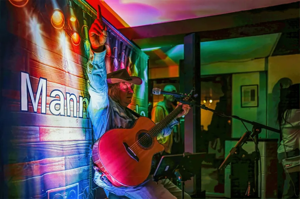 Mannie Live auf der Bühne mit Gitarre, energische Geste und Bühnenlicht